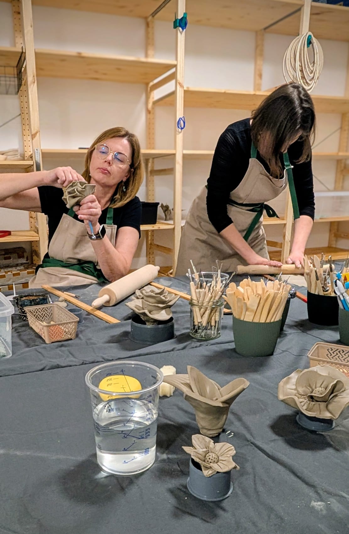 Dwie uczestniczki lepiące kwiaty z gliny przy stole warsztatowym